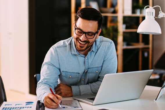 A man in a blue shirt, working at a laptop in an office